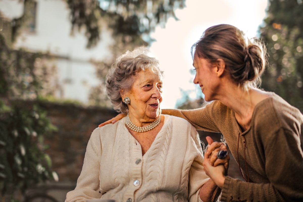 A warm moment between an elderly woman and her support person holding hands outdoors