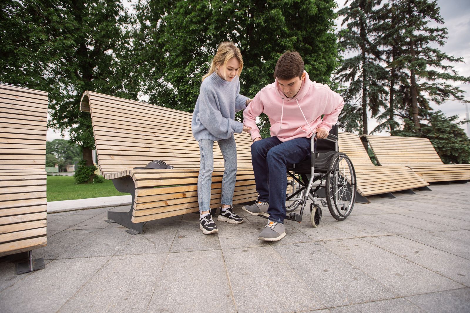 A support worker walking alongside a young man using a wheelchair in a sunny park